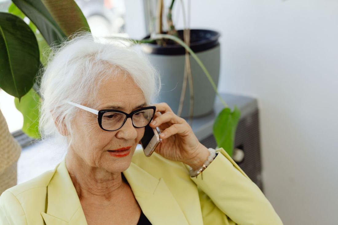 An older woman with glasses talking on her phone at home