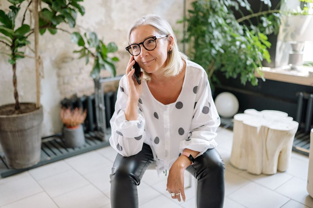 A smiling woman talking on her phone at home among plants